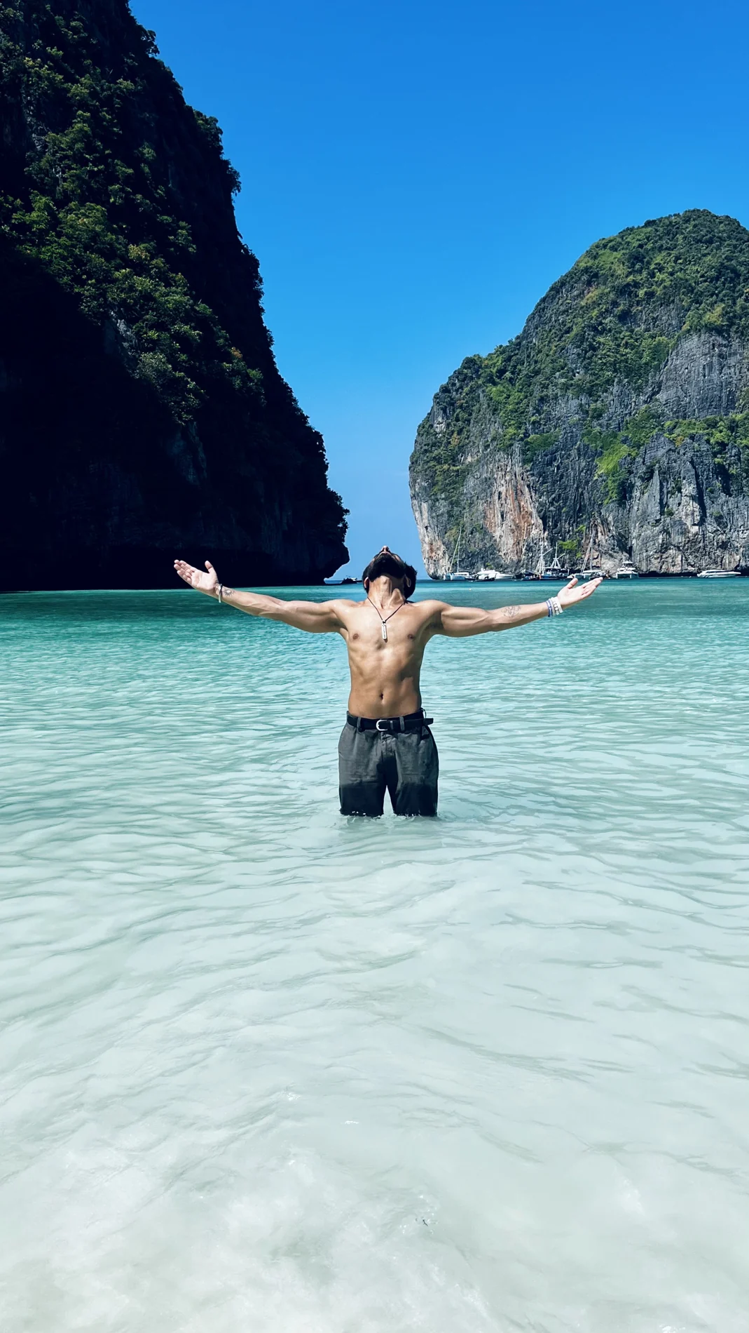 Shubham standing in clear turquoise sea between tall coastal cliffs