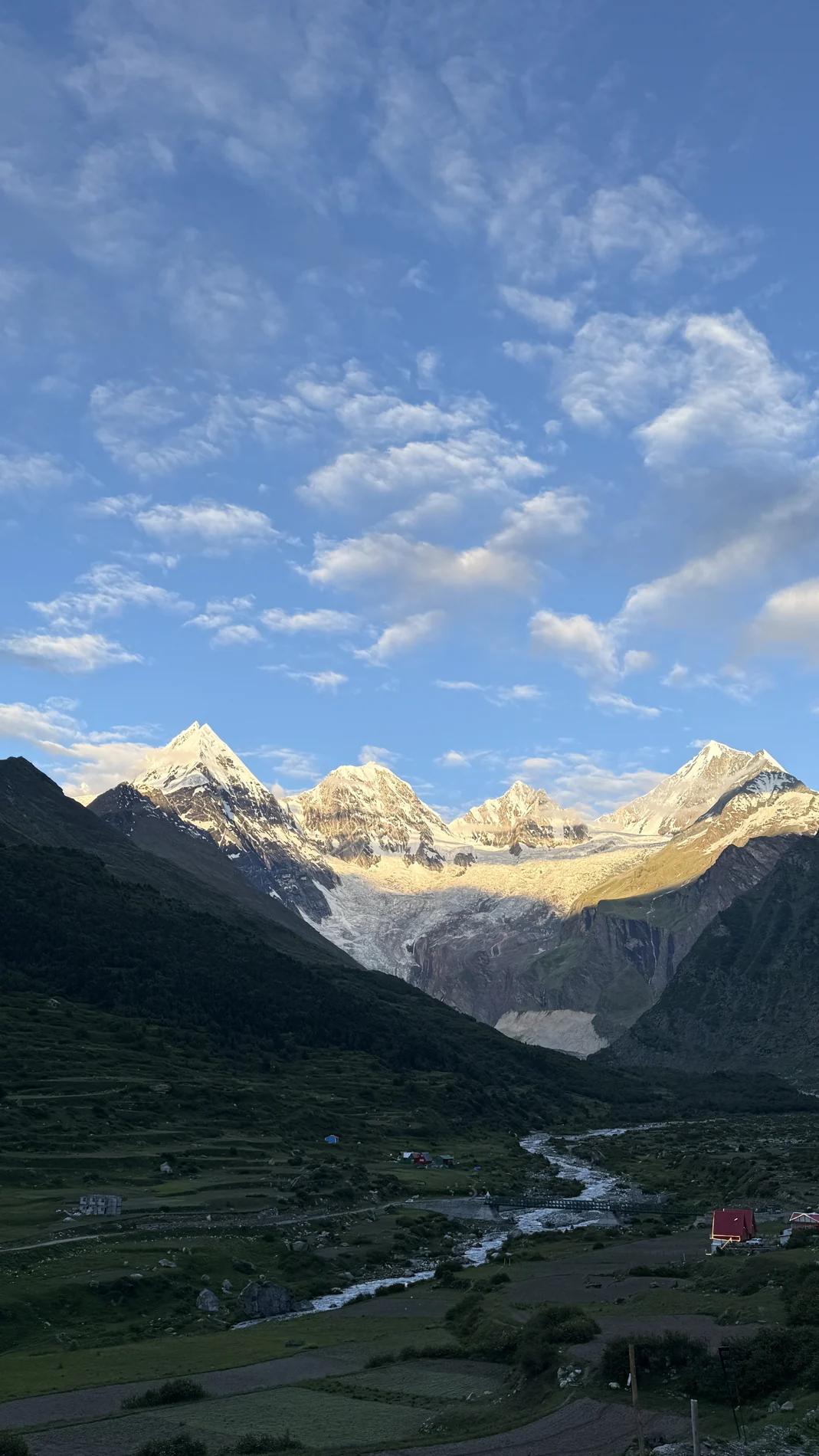 Sunlit mountain peaks above a green valley and winding river
