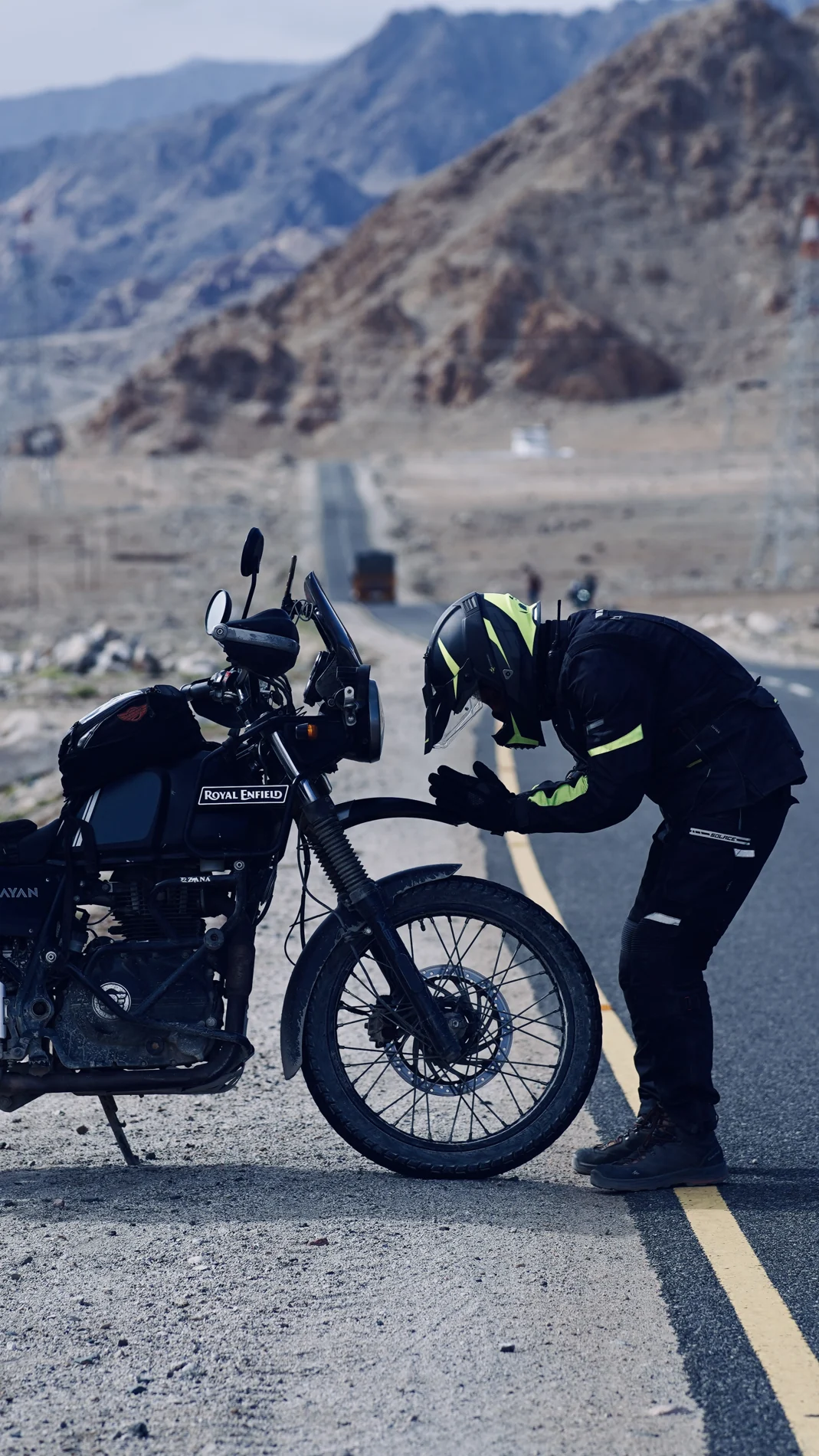 A helmeted rider leaning towards a motorcycle on an open mountain road