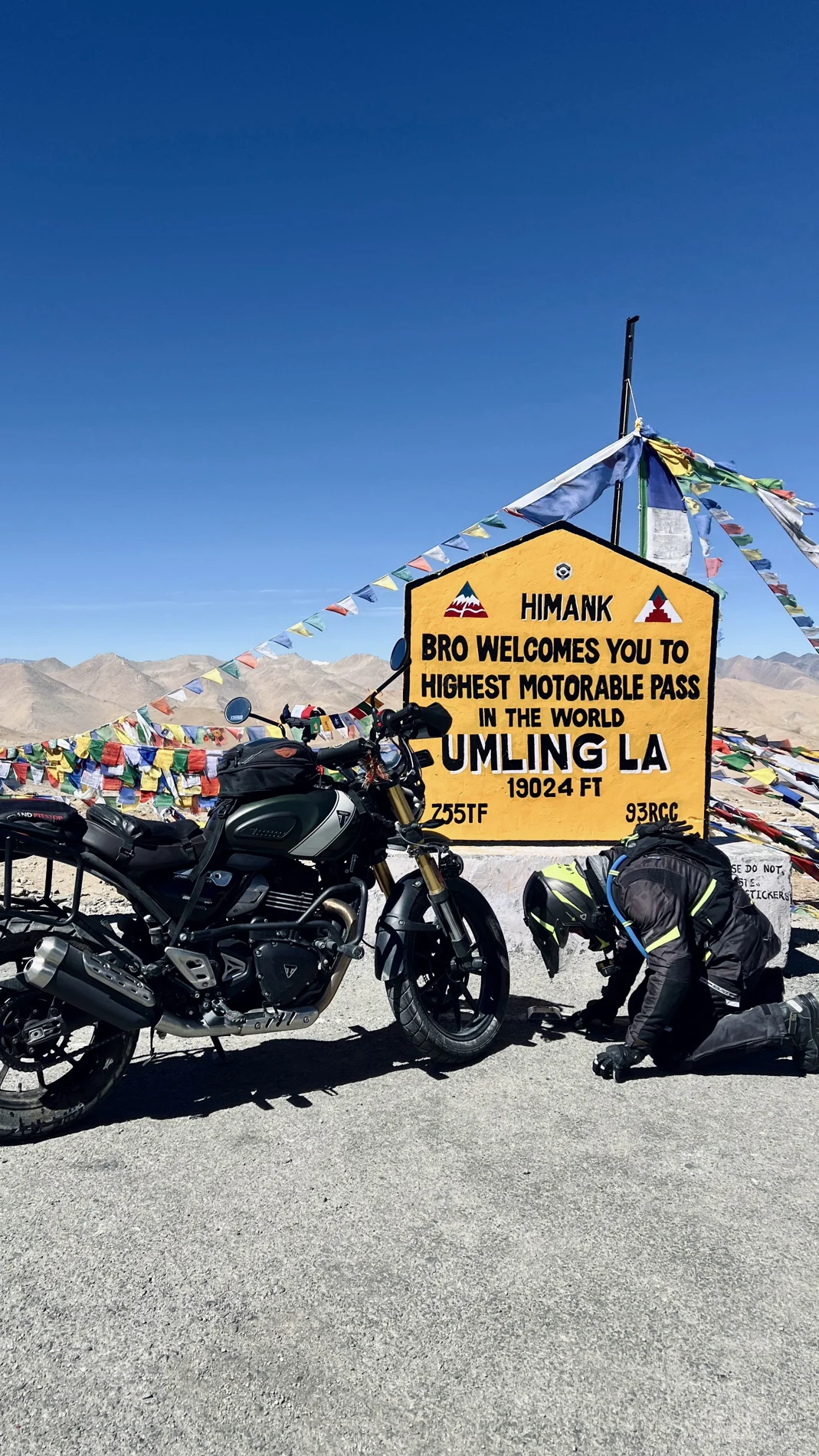 Motorcycle and rider beside the Umling La sign and prayer flags